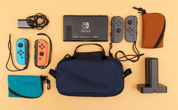 A Navy Parapack Grab Bag with Nintendo Switch and accessories next to it, including two Mini Ghost Whale Pouches.